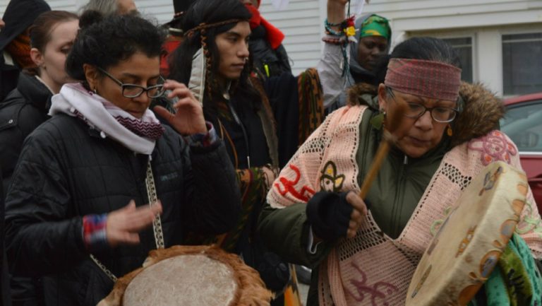 Picture of two Indigenous women beating drums in the streets as part of a gathering